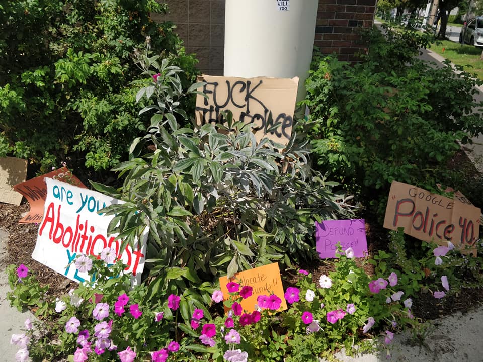 Hand-made signs in bushes. Text Reads - Are you abolitionist yet?, Defund Police, Google Police 40%